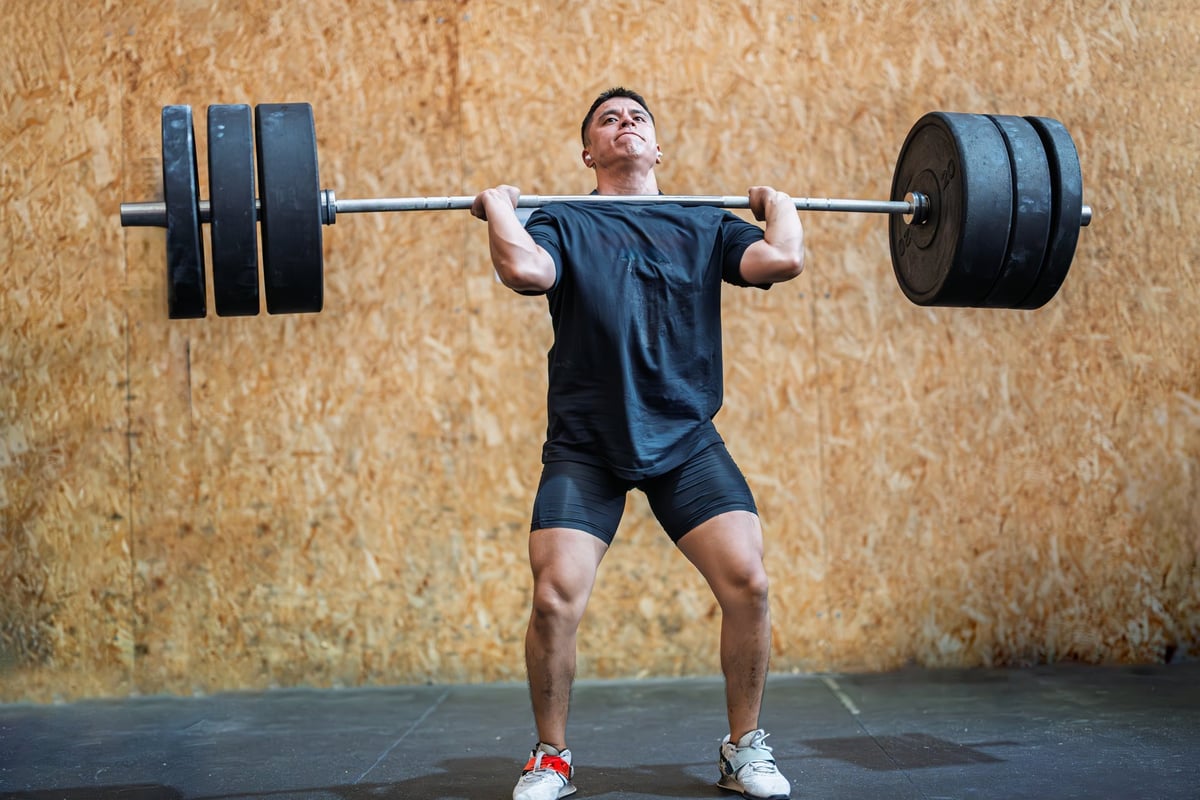 An athlete lifts a heavy barbell overhead with determined focus in a modern gym setting during a training session