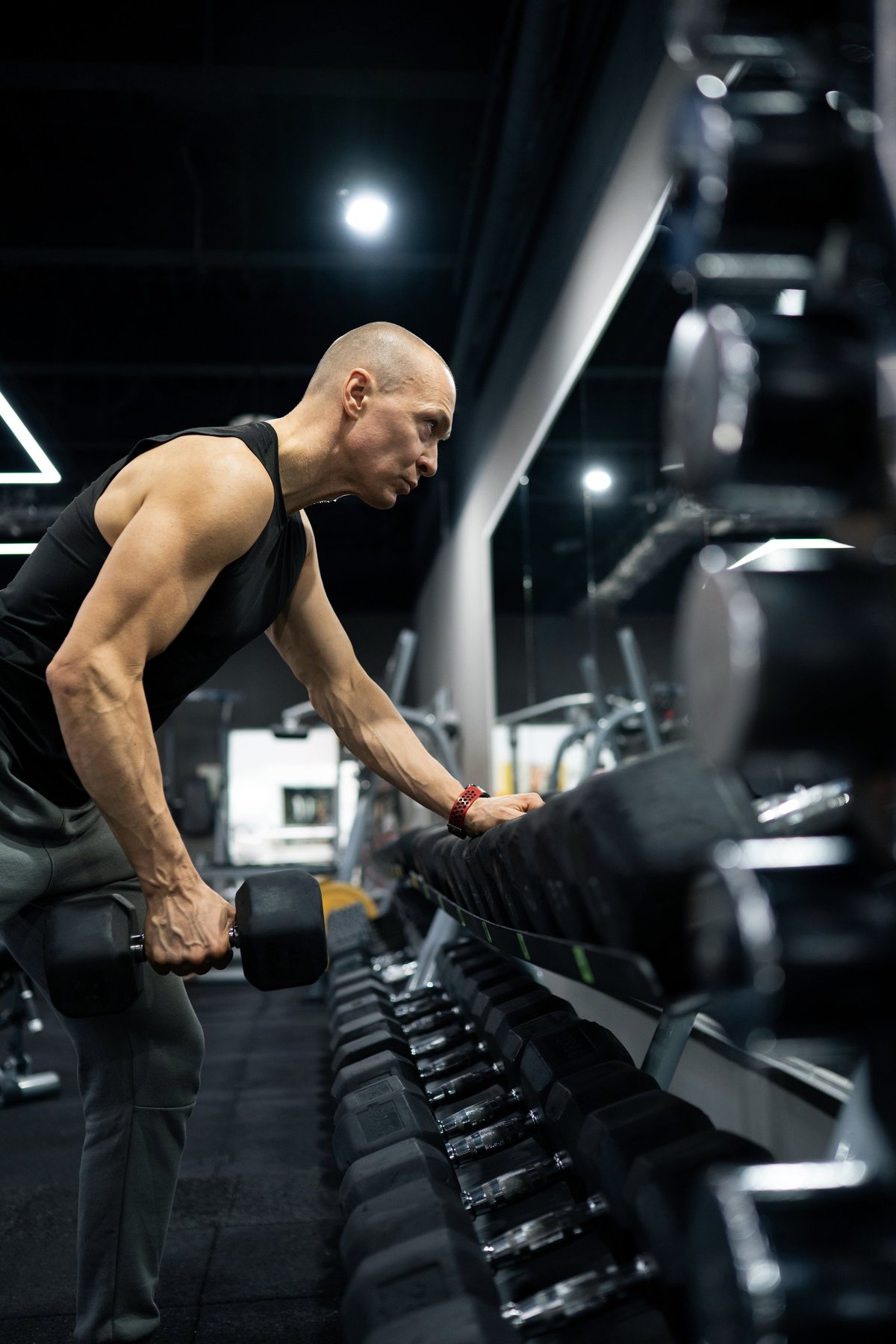 Muscular athletic man performing one arm dumbbell row exercise in modern fitness gym. Strength training, bodybuilding and healthy lifestyle concept